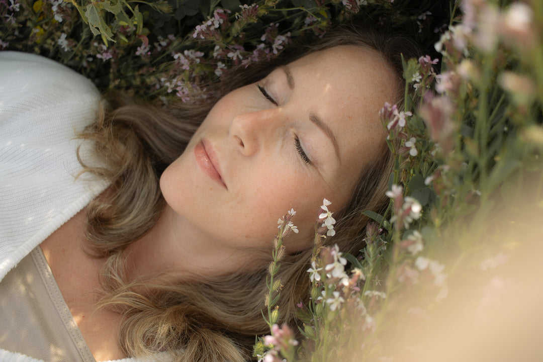 Therese Håkansson, Swedish artist and founder of BabyBlossom Art Design, resting peacefully among delicate wildflowers in a soft, nature-inspired setting.
